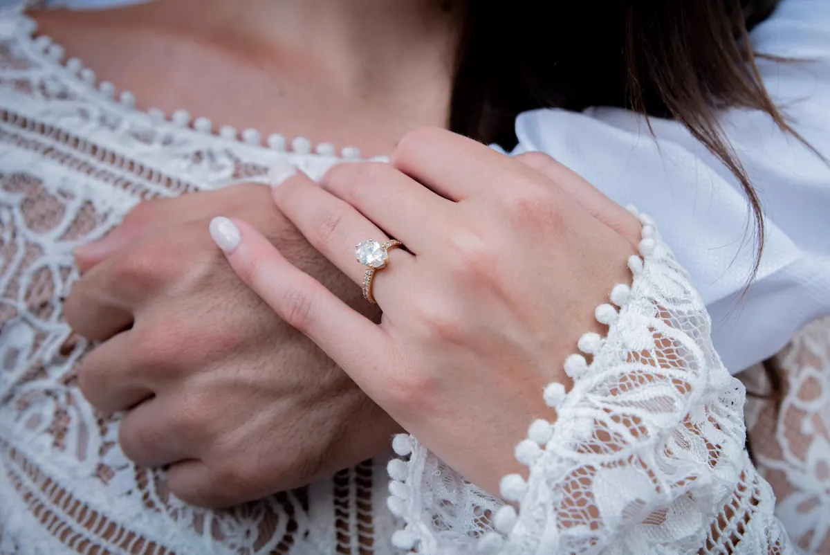 A hand wearing a gold engagement ring, held close to the light.