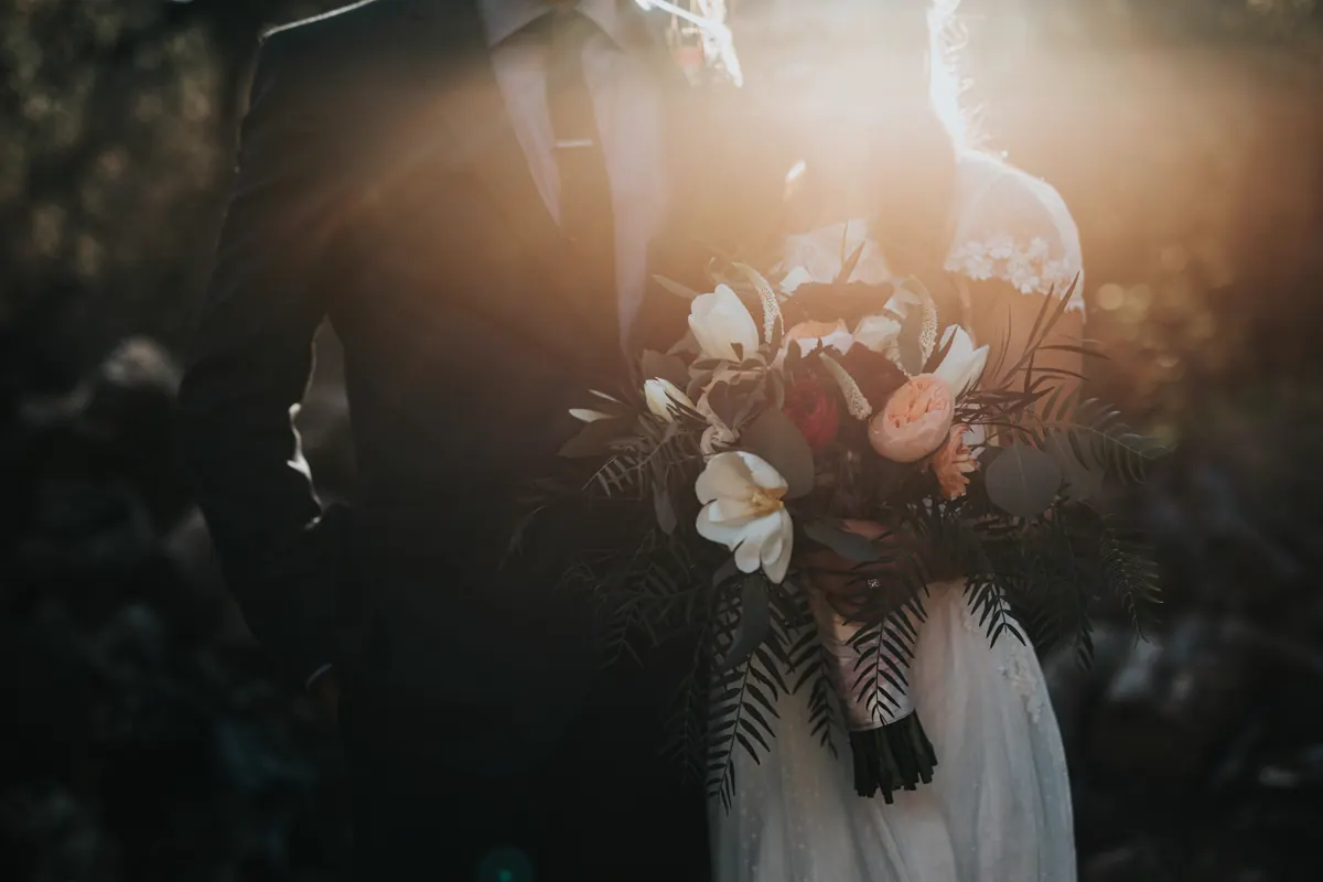 A groom standing beside his bride, who is holding a bouquet.