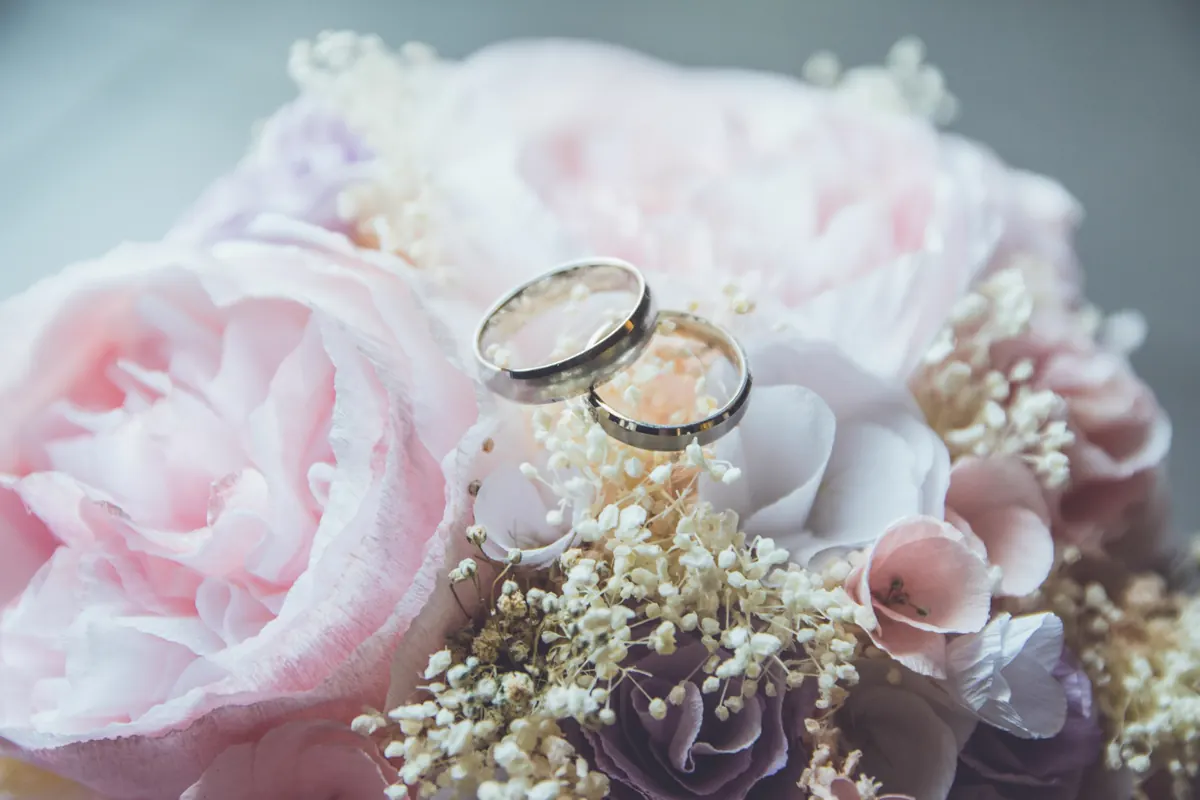 A pair of gold wedding rings resting on pink roses.